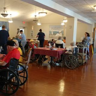 A bustling dining area in a nursing home with residents and caregivers engaging in activity.