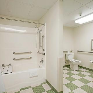 An accessible bathroom featuring a shower with grab bars, a toilet, and a sink, all within a tiled space.