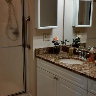 A well-organized bathroom featuring a granite countertop with a sink, mirrors, and a shower enclosure.