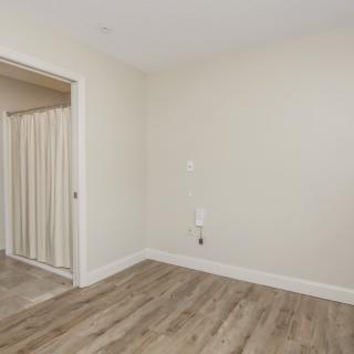 An empty room with wood flooring and white walls, featuring a doorway with a curtain.