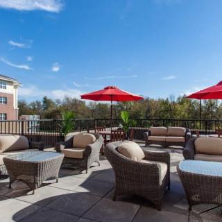 A spacious outdoor patio with wicker furniture and red umbrellas under a clear blue sky.