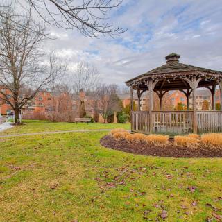 A serene park scene featuring a wooden gazebo surrounded by grass and trees under a cloudy sky.
