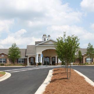 A view of a large building with a driveway and landscaped surroundings under a cloudy sky.