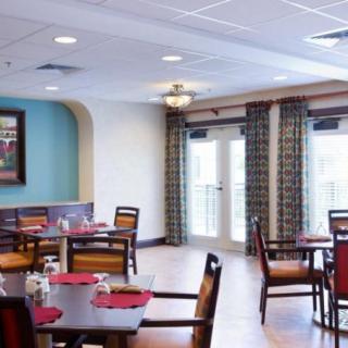A cozy dining area with neatly arranged tables and chairs, featuring warm lighting and large windows.