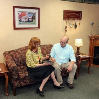 Two people sitting on a couch having a conversation in a living room setting.