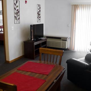 A cozy living room with a dining area, featuring a sofa, TV, and a window with curtains.