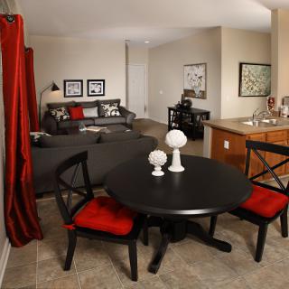 A modern living and dining space featuring a black table with red chairs, complemented by a cozy grey sofa and stylish home decor.