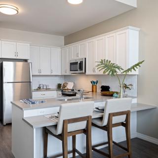 A modern kitchen with white cabinets and a central island, featuring stainless steel appliances and bar stools.