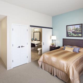 A modern bedroom with a bed, nightstand, and an adjacent bathroom.