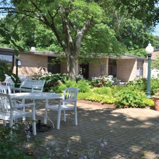 A peaceful garden patio with outdoor furniture and lush greenery on a sunny day.