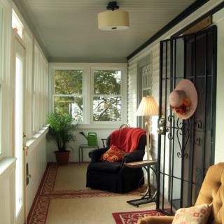 A cozy porch with a comfortable armchair, lamp, and potted plant.