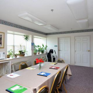 A tidy meeting room setup with a conference table, chairs, folders, and indoor plants.
