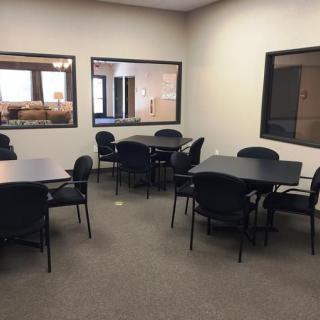 A simple office meeting room with tables and chairs arranged for group discussions.