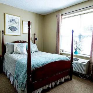 A cozy bedroom featuring a four-poster bed with patterned bedding, decorative wall art, and a window with curtains providing natural light.