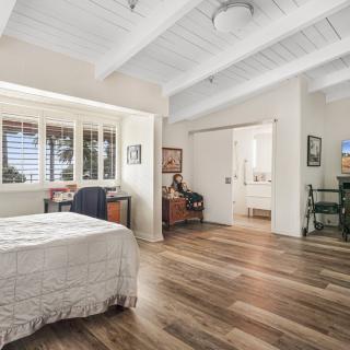 A cozy bedroom with wood flooring, ceiling beams, and ample natural light.
