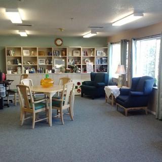 A cozy living room with a table, chairs, bookshelves, and large windows.