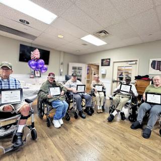 A group of elderly men in wheelchairs proudly displaying their certificates during a celebratory event.
