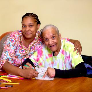 A joyful moment shared between a caregiver and an elderly person as they engage in an art activity together.