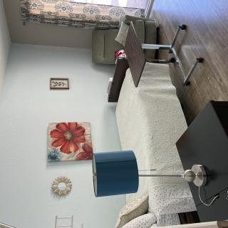 A neatly arranged room featuring a single bed, blue lamp on a side table, and a flower painting on the wall.