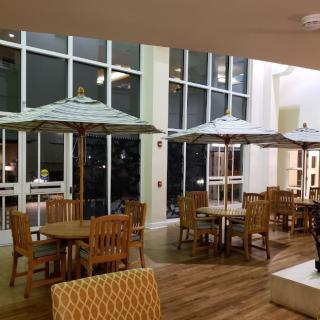 A spacious indoor seating area with wooden tables and chairs, featuring large umbrellas and floor-to-ceiling windows.