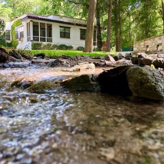 A peaceful stream flows by a house nestled in the forest.