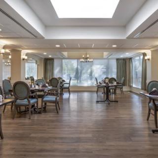 A spacious dining room with elegant decor, featuring multiple tables and chairs, large windows, and wooden flooring.
