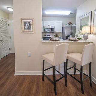A modern kitchen with a counter and two tall stools, featuring stainless steel appliances and warm lighting.