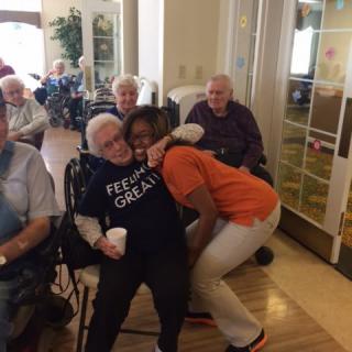 A joyful moment shared between an elderly resident and a caregiver in a nursing home setting.