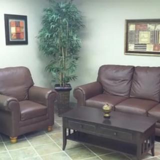 A cozy living room with a brown leather sofa, armchair, coffee table, indoor plant, and wall artwork.