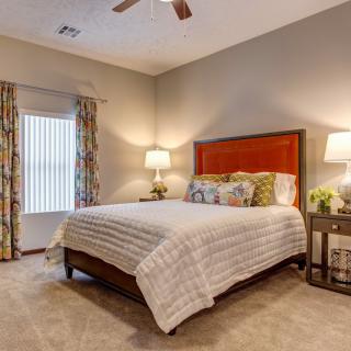 A cozy bedroom with a neatly made bed, warm lighting, and patterned curtains.