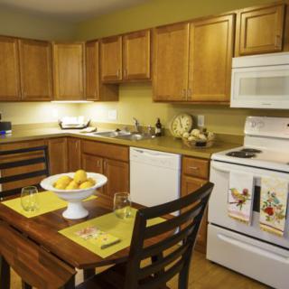 A cozy kitchen with wooden cabinets, a dining table set for two, and modern appliances.