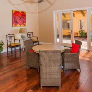 A cozy dining area featuring wicker chairs and a round table, complemented by vibrant artwork and warm hardwood floors.