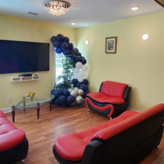 A cozy living room with red and black seating, adorned with a balloon arrangement and featuring a large television on the wall.