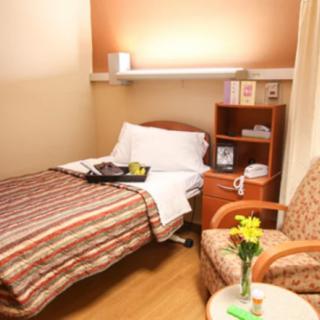 A cozy hospital room with a single bed, comfortable chair, and flowers on a small table.