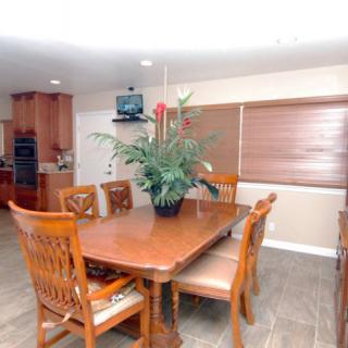 A dining area with a wooden table and chairs, featuring an indoor plant centerpiece, adjacent to a kitchen.
