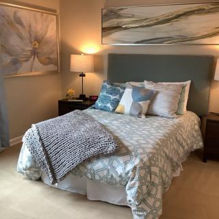 A cozy bedroom with a neatly made bed, decorative pillows, two bedside lamps, and wall art.