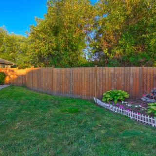 A backyard garden with a wooden fence, lush green lawn, and well-maintained vegetation.