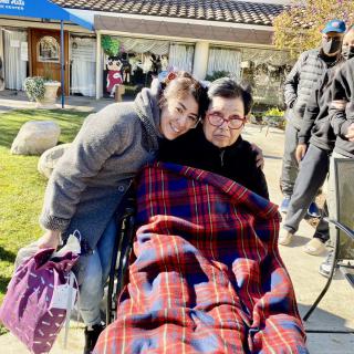 Two people enjoying a sunny day outdoors, one sitting in a wheelchair covered with a blanket.