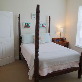 A cozy bedroom featuring a four-poster bed with white bedding, complemented by a nightstand and lamp.