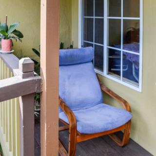 A cozy porch corner featuring a cushioned chair and potted plants.
