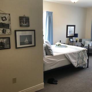 A cozy bedroom featuring a neatly made bed, wall art, and comfortable seating.
