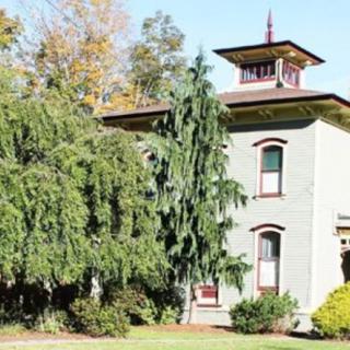 Historic house with a tower surrounded by lush trees.