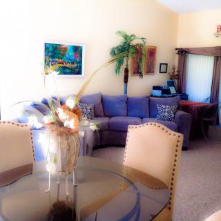 A cozy living room featuring a large corner sofa, a dining table with chairs, and decorative elements like artwork and a potted plant.