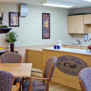 A cozy cafe interior with a kitchen and dining area, featuring wooden tables and chairs.