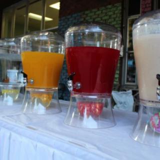 A row of beverage dispensers filled with colorful juices at an outdoor event.