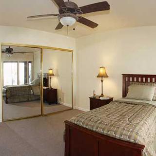 A cozy bedroom featuring a bed, bedside lamp, mirrored closet doors, and a ceiling fan.