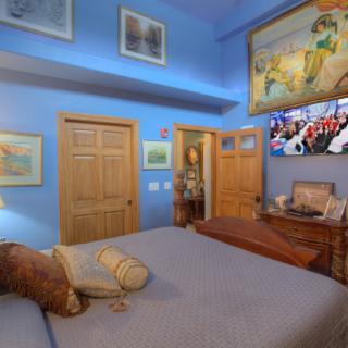 A cozy bedroom with blue walls adorned with various artworks and a neatly made bed.