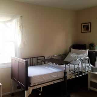 A hospital room with a single bed and medical equipment, illuminated by natural light from the window.