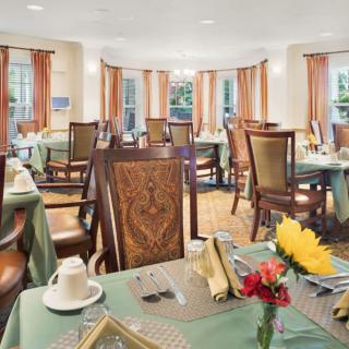 An elegant dining room with neatly arranged tables and chairs, featuring tableware and floral decorations.