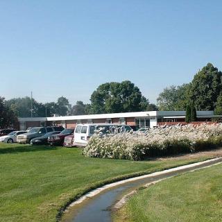 A building surrounded by a parking lot, well-maintained grass, and flowerbeds under a clear blue sky.